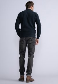 Donkere gebreide trui met een kraag, grijze spijkerbroek en bruine leren laarzen. Heeft een gestructureerde stof en een getailleerd ontwerp.