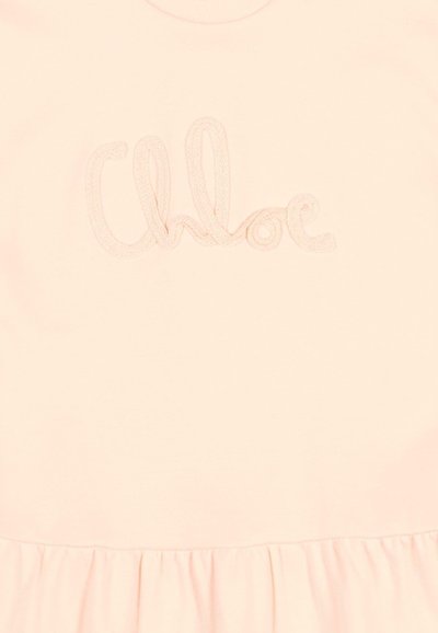 Tissu rose clair avec le mot « Chloé » brodé en fil assorti au-dessus d'une couture froncée.