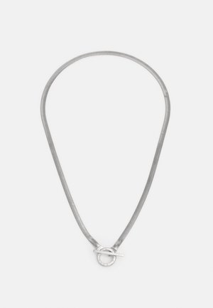 Collier chaîne ton argent avec un fermoir toggle rond, posé à plat sur un fond blanc.