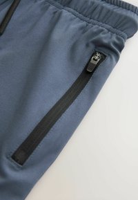 Donkerblauwe sportbroek met een gladde textuur, voorzien van een ritszak met zwarte accenten en een elastische tailleband voor een comfortabele pasvorm.