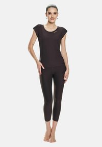 Top scurt negru cu maneci scurte și guler rotund, accentuat cu auriu, asociat cu leggings negri până la jumătatea gambei, ambele realizate dintr-un material neted și elastic.