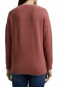 Pull en maille gaufrée rose poussiéreux avec une coupe décontractée, un col rond et des poignets côtelés, associé à un jean bleu. Présente un tissu texturé.