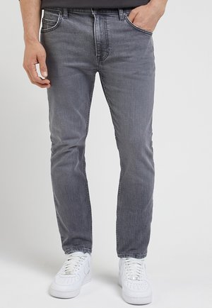 Jean en denim gris avec une coupe droite, un design à cinq poches et un léger délavage. Équipé d'une fermeture éclair et de passants de ceinture. Assorti à des baskets blanches.