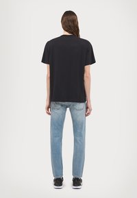 T-shirt nera in cotone a maniche corte, vestibilità comoda e colletto rotondo, abbinata a jeans dritti blu chiaro e sneakers nere.