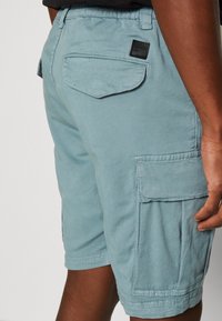 Ljust blå cargoshorts gjorda av bomullsblandat tyg, med en bakficka och en sidocargoficka med sydda detaljer.