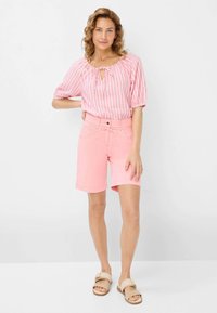 Lichtroze, knielange shorts met een tailleband en zakken, gecombineerd met een gestreepte roze blouse met een ronde halslijn en strikdetail.