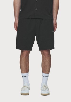 Shorts noirs texturés avec une ceinture élastique, associés à des chaussettes blanches montantes et des baskets blanches. Pas de logos ou de motifs visibles sur les shorts.