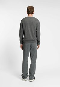 Maglione grigio con maniche lunghe, scollo rotondo e polsini a costine, abbinato a pantaloni grigi chiari con tasche laterali e una vestibilità morbida.