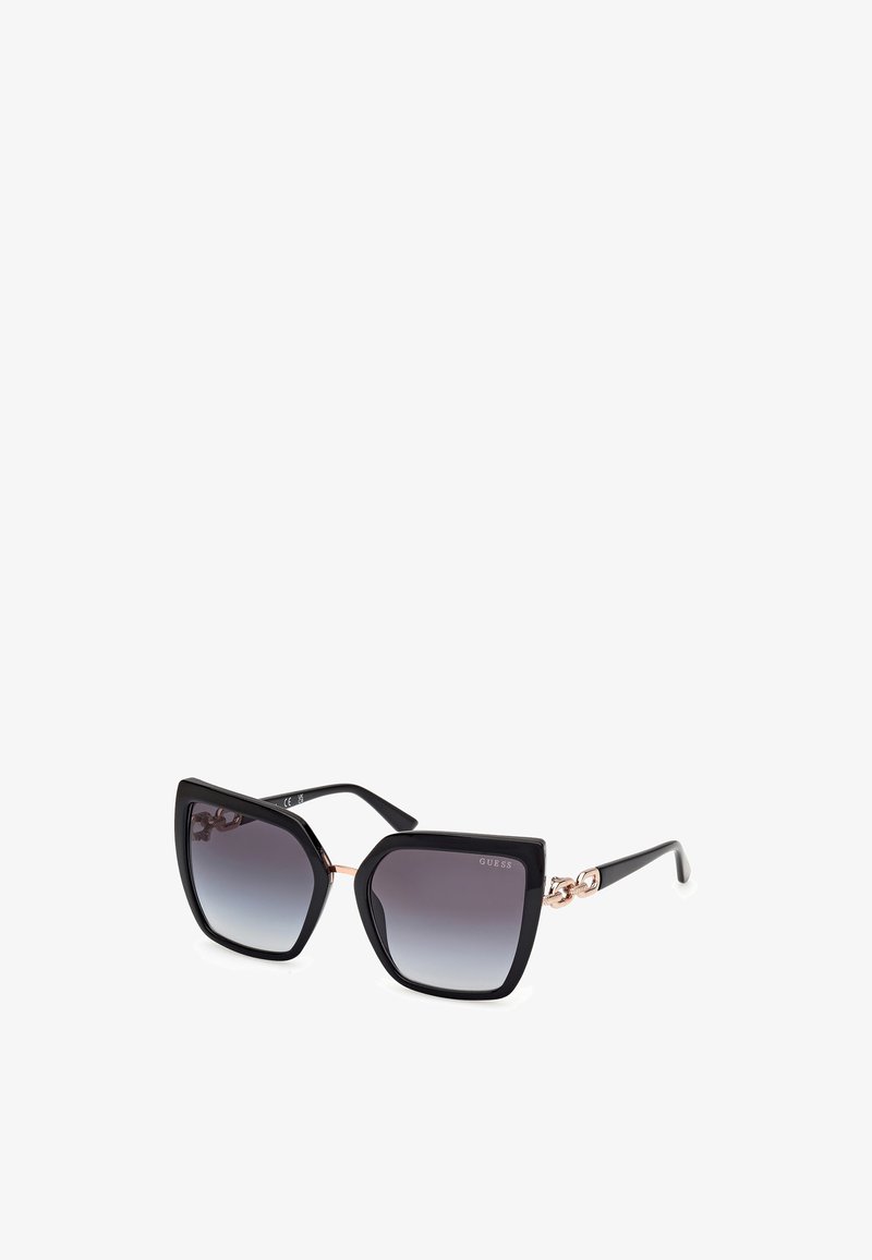 Cat-eye sunglasses with a glossy black frame, gradient gray lenses, and a gold chain accent on the temples. Bold and geometric design.