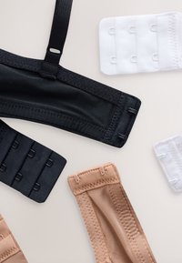 Czarne i beżowe ramiączka do biustonosza z przymocowanymi haczykami oraz białe przedłużki do biustonosza ułożone na jasnej powierzchni.