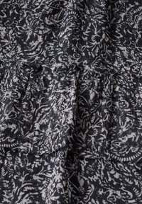 Tissu �à motifs noir et blanc avec un motif florale, présentant une texture froissée et des détails de volants subtils le long de la couture.