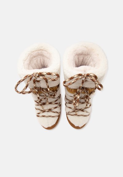 Ζευγάρι λευκών χνουδωτών χειμερινών μπότες με καφέ και λευκά κορδόνια με σχέδιο, από πάνω σε απλό φόντο.
