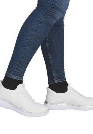 Weiße Sportschuhe mit strukturiertem, netzartigem Design, silbernen Akzenten und dicken Sohlen, kombiniert mit dunklen Socken und blauen Jeans.