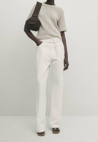 Valkoiset leveälahkeiset housut, joissa on kiristysnyöri vyötäröllä, yhdistetty lyhythihaiseen pilkulliseen beigen sävyiseen puseroon ja tummanruskeaan olkalaukkuun.