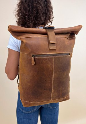 Brown leather roll-top backpack with a zippered front pocket, sturdy handle, and contrasting stitching. Durable and functional design.