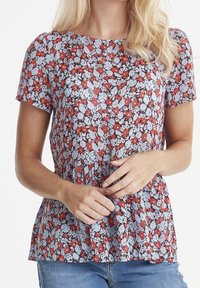 Haut fleuri à manches courtes, présentant un motif de fleurs rouges et bleu clair sur un fond noir, avec un ourlet froncé de style peplum.
