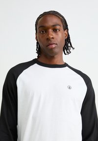 Sort og hvid langærmet T-shirt med raglan-design, der har et lille logo på brystet og en glat bomuldsstruktur.