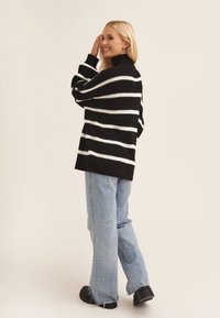 Black and white striped oversized sweater with a high neck, paired with light blue wide-leg jeans and black chunky shoes.