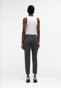 Grijze taps toelopende broek met een elastische tailleband, twee achterzakken, gecombineerd met een witte mouwloze top. Zachte textuur, minimalistisch ontwerp.