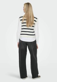 White knitted vest with black stripes, layered over a white shirt, paired with loose-fitting gray trousers and sneakers. Long straight hair visible.