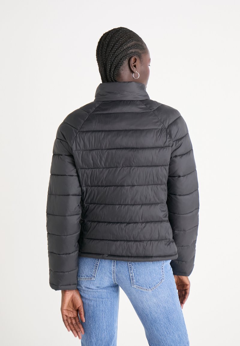 Chaqueta de plumas negra con acolchado horizontal, cuello alto y mangas largas, combinada con jeans de color azul claro.