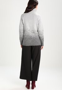 Sweter w odcieniach szarości i bieli z wysokim kołnierzem i długimi rękawami, zestawiony z czarnymi szerokimi spodniami. Sweter ma fakturowany wzór.