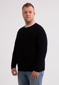 Maglione nero a maniche lunghe in tessuto morbido, con scollo a girocollo e vestibilità rilassata, abbinato a jeans azzurri chiari.