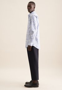 Camicia azzurro chiaro a maniche lunghe con motivo floreale, abbinata a pantaloni e scarpe nere, che evidenzia un taglio moderno e rilassato.