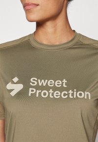 Maslinasto zeleni atletski majica s kratkim rukavima, s istaknutim bijelim logotipom i natpisom "Sweet Protection", glatka tekstura.