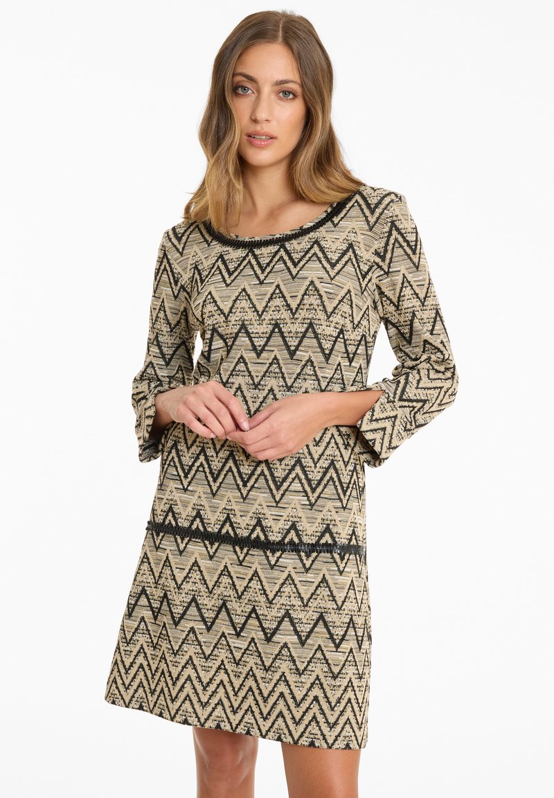 Beiges Kleid mit einem schwarzen Zickzack-Muster, rundem Ausschnitt und Dreiviertelärmeln. Strukturierter Stoff mit lockerer Passform.