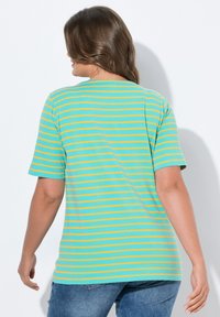 Camiseta de manga corta en color teal con rayas amarillas horizontales; cuello redondo estándar y tejido suave con un corte relajado. Diseño visible en la parte posterior.