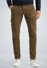 Bruine cargobroek van textielstof, met meerdere zakken en zichtbare stiksels. Draagt met witte sneakers voor contrast.
