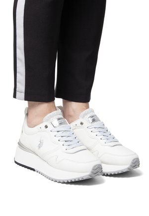 Białe sportowe sneakersy z gładką syntetyczną cholewką, srebrnymi akcentami i teksturowaną podeszwą. Sznurowany design z siateczkowym językiem i detalem logo.