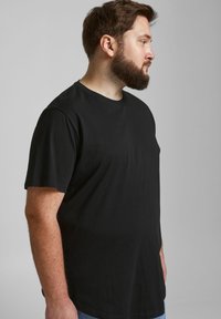 Mustat puuvillaiset T-paidat, joissa on pyöreä kaula-aukko, lyhyet hihat ja rento istuvuus, esillä sivukulmassa vaaleanharmaata taustaa vasten.