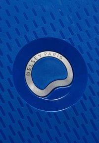 Materiale della valigia blu con superficie testurizzata caratterizzata da scanalature parallele. Logo circolare argento centrato su uno sfondo circolare blu scuro.