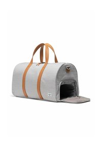 Sac de sport gris clair avec des sangles en cuir brun, forme arrondie, fermeture éclair et rabat d'accès ouvert. Présente une étiquette en tissu sur le côté.