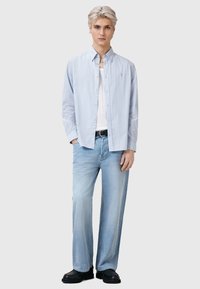 Lys blå stribet skjorte med knapper over en hvid tanktop, paired med løse lys blå denimjeans og sorte sko.