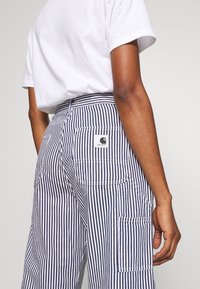 Spodnie cargo w paski w kolorze granatowym i białym, wyposażone w liczne kieszenie, wysoki stan oraz wytrzymałą tkaninę z kwadratową naszywką z logo z tyłu.