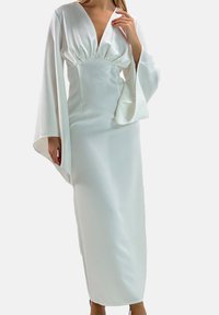Witte satijnen maxi-jurk met een diep V-hals, geplooide top en brede klokkende mouwen. Soepele textuur en een strakke, slanke pasvorm.