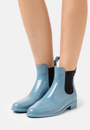 Bottes cheville brillantes bleues avec une finition élégante, des panneaux latéraux élastiques et un petit talon bloc. L'intérieur est doté d'une doublure noire.