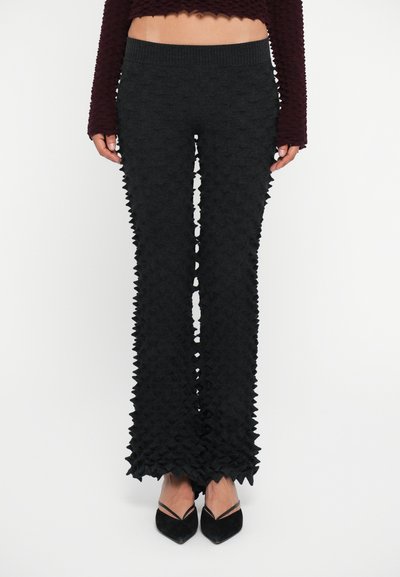 Pantalones negros hechos de una tela texturizada con un diseño dentado a lo largo de los lados; cuentan con una cinturilla elástica alta y un corte acampanado.