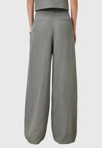 Široké kalhoty v světle šedé lněné látce. Mají vysoký pas, dvě zadní kapsy a hladkou texturu s minimálními švy.