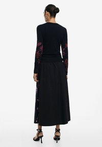 Top a maniche lunghe nero con ricami floreali sulle maniche, abbinato a una gonna maxi nera coordinata. Indossato con tacchi alti con cinturini.