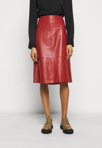 Falda midi de cuero rojo con textura suave, que presenta una cintura alta y costuras sutiles, combinada con zapatos marrones de cordones.