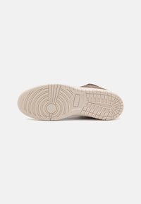 Podeszwa sneakersów wykonana z gładkiego, beżowego materiału gumowego z teksturowanym wzorem, w tym koncentrycznymi okręgami i prostokątnymi uchwytami dla lepszej przyczepności.