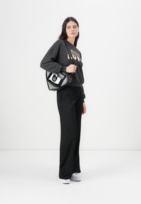 Felpa nera con stampa dorata "LOVE", pantaloni neri a gamba larga, sneakers bianche e una borsa nera con hardware argentato e accenti a contrasto.