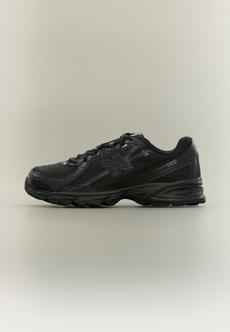 Baskets de sport noires avec tige en mesh, fermeture à lacets, semelle rembourrée et logo de la marque sur le côté et le talon, montrées en profil latéral.