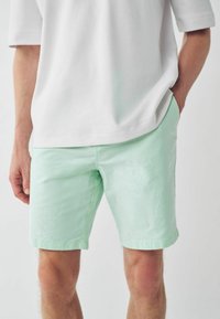 Shorts de un verde mentă deschis, realizate dintr-un material texturat, cu buzunare laterale și un tiv drept, asortate cu o cămașă albă, cu o croială lejeră.