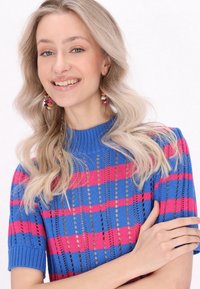 Pletený top s krátkým rukávem v modré barvě se růžovými pruhy, s texturovaným vzorem a žebrovaným výstřihem. Mezi detaily najdete výřezy a přiléhavý střih.