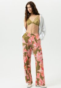 Olijfgroene bralette met kanten details, gecombineerd met lichtgewicht, wijde broek met een roze bloemenpatroon op een donkere achtergrond.